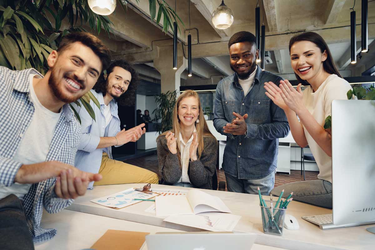 Group of co-workers clapping and cheering around desk.